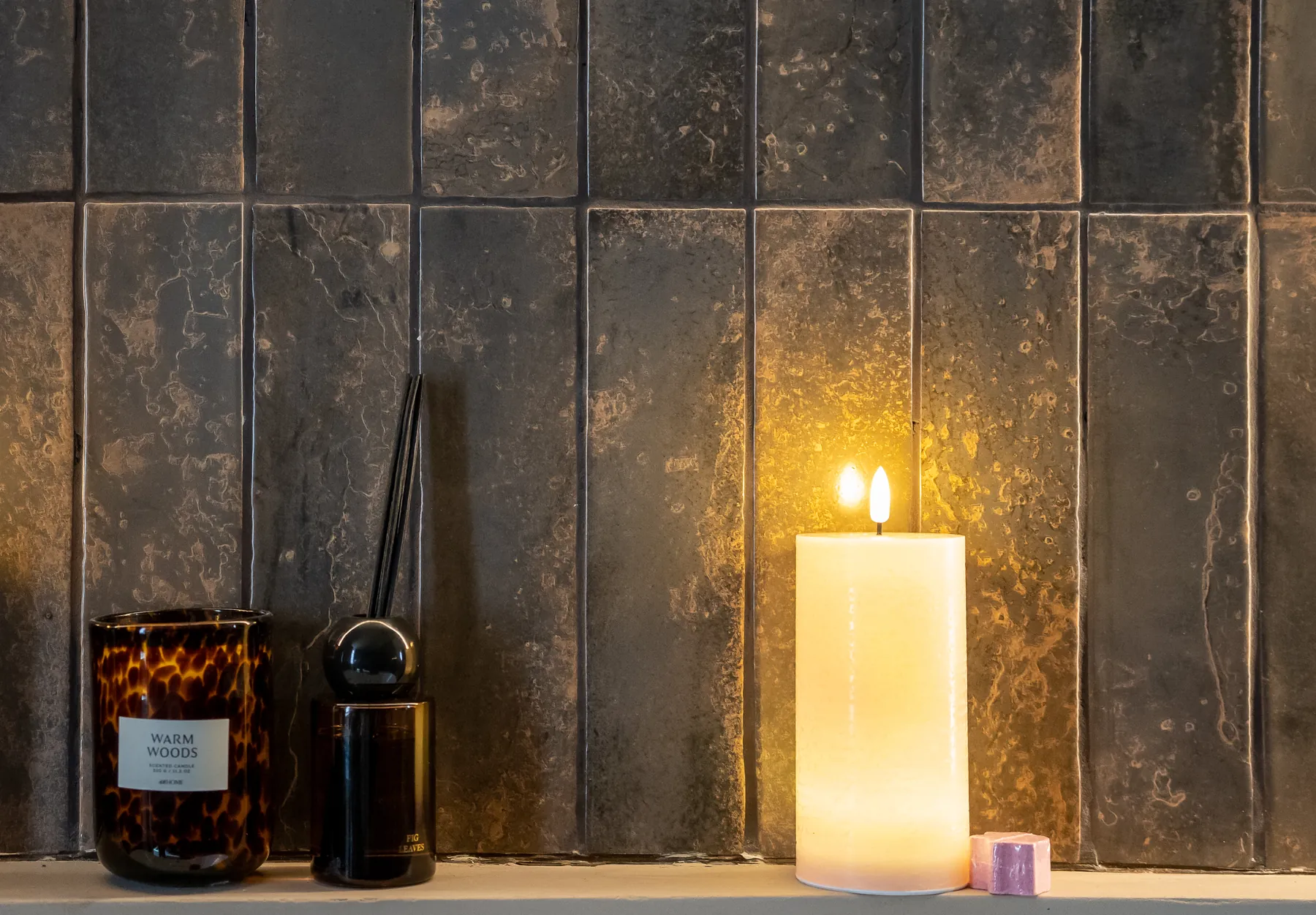 Bougie LED crème en cire véritable avec flamme réaliste devant un mur carrelé