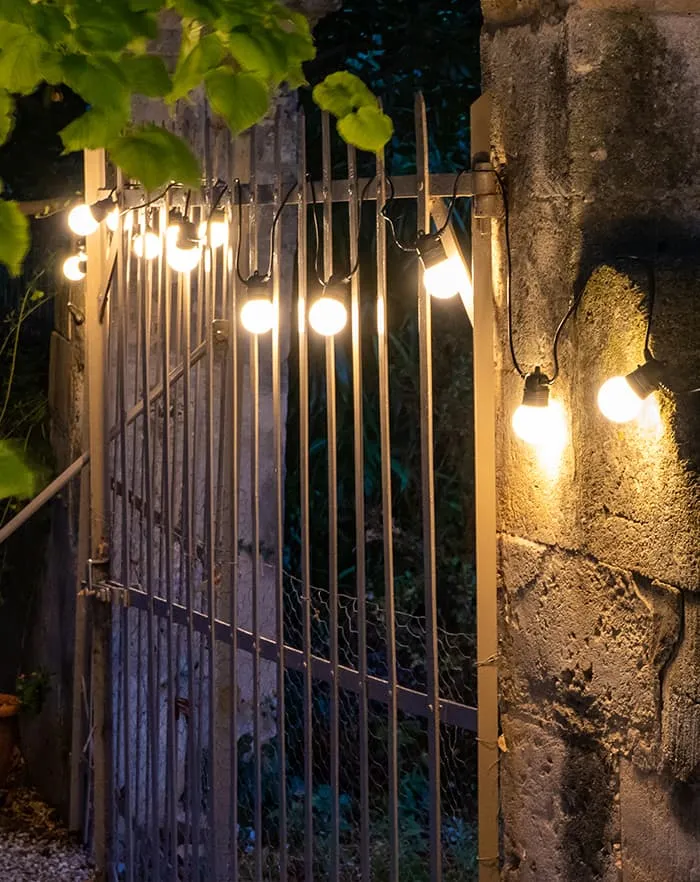 Guirlande guinguette solaire allumée sur un portail en pierre, la nuit