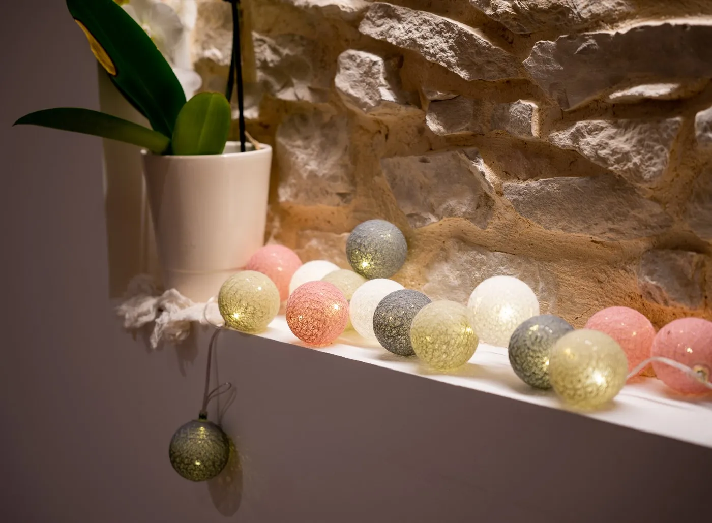 Guirlande lumineuse à boules de coton pastel sur un rebord en pierre
